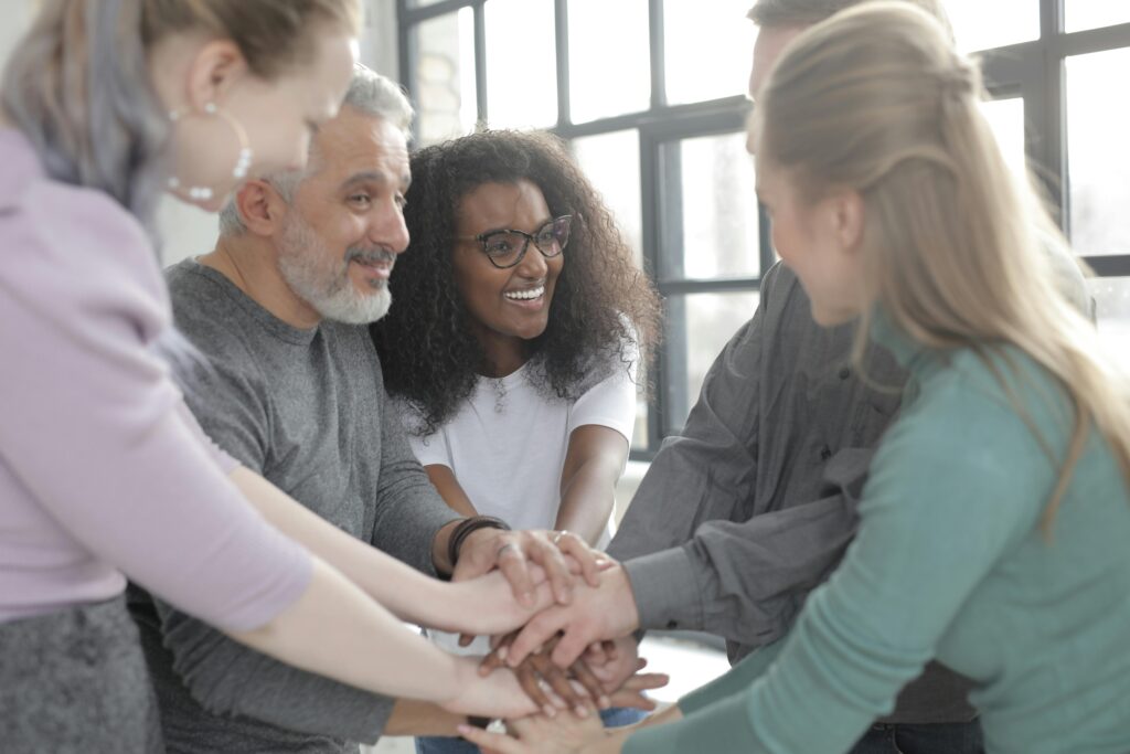 A diverse group of adults engaged in a cheerful team-building exercise inside an office setting.